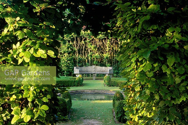 View through opening in beech hedge to green garden at Cranbourne Manor in Dorset