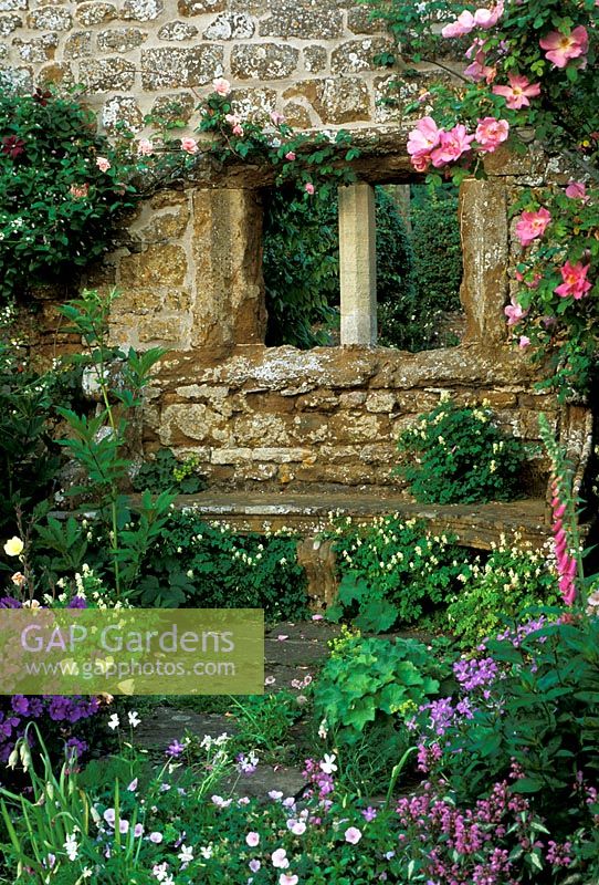 Window on old wall with climbing rose and stone bench at Broughton Castle in Banbury