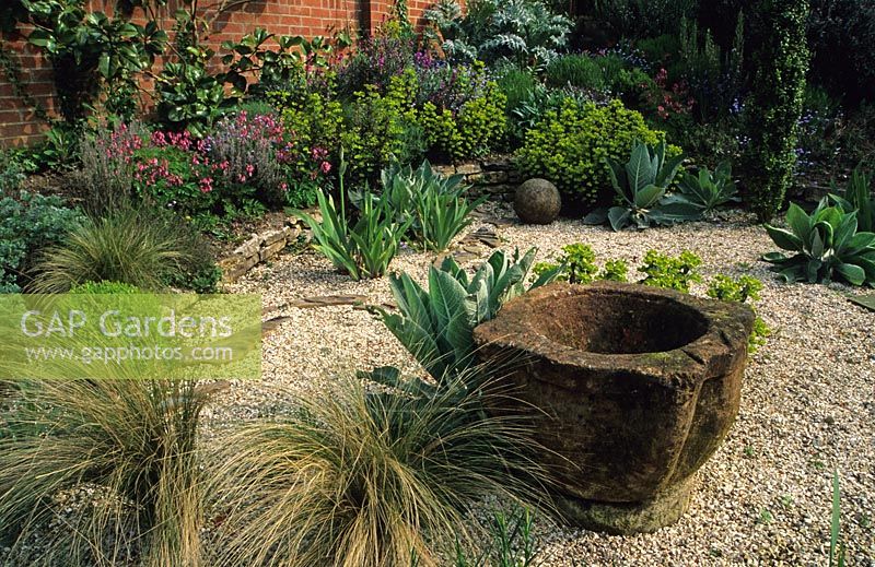 Dry gravel garden with grasses, Euphorbia and mortar sculpture at Thursley Lodge in Surrey