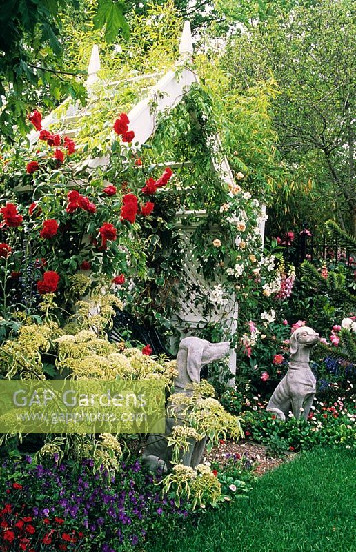 Rose covered seat with climbing roses and dog statues. Cornus controversa 'Variegata' and Rosa 'Pauls Scarlet'. Chelsea FS 1997