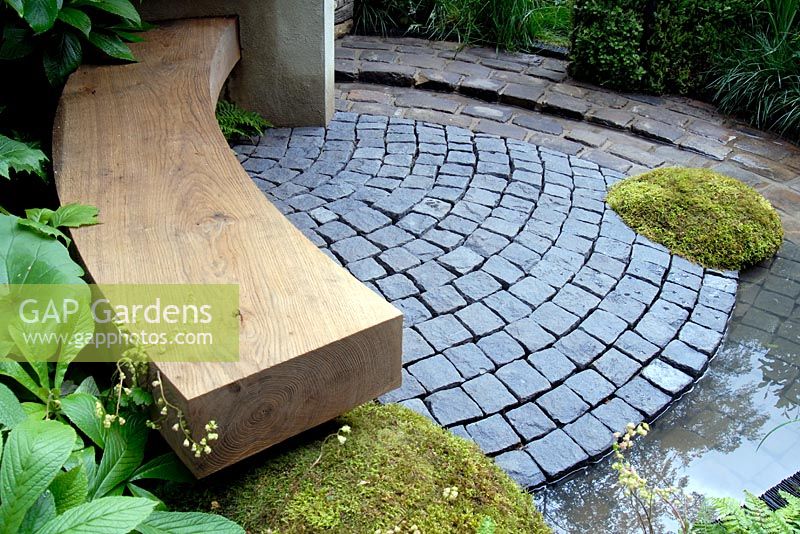 An oak bench and patio paved with cobble setts and water feature rill 