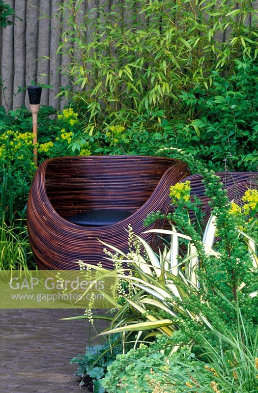 Contemporary wicker seat with green planting including bamboo, Euphorbia and Phormium 'Cream Delight'. 'Walking Barefoot with Bradstone' Garden, Chelsea Flower Show 2006.