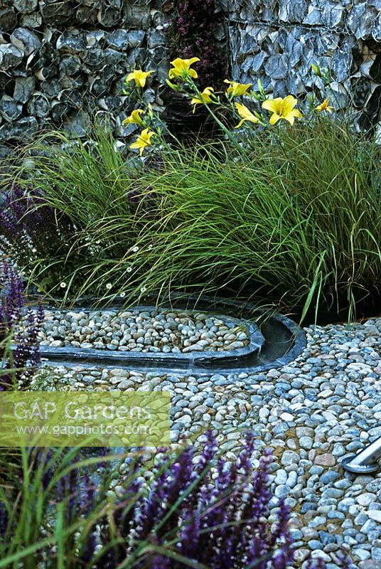 Time Line Garden at Hampton Court Flower Show 2006 designed by Emma Dawson from Capel Manor College - Erigeron karvinskianus, Salvia nemorosa 'Ostfriesland' Hemerocallis and Stipa arundinacea by meandering beaten lead stream course with pebble patio and pebble gabion wall 