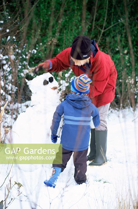 Mother and child making snowman in snow-covered garden