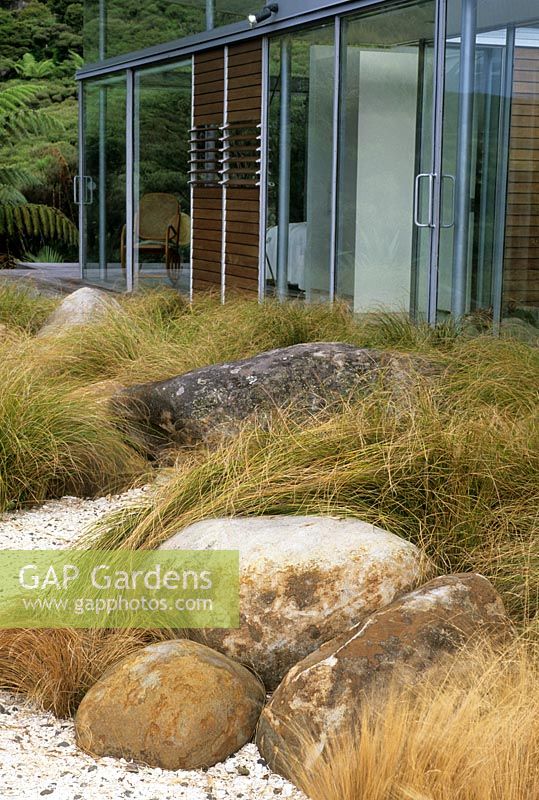 Garden view with boulders and native grasses contrasting with modern building at Piha, New Zealand. Garden Design - Ted Smyth. 
