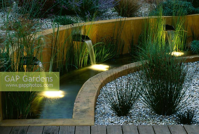 Gravel garden with water rill, rendered concrete walls and three spouts lit up at night