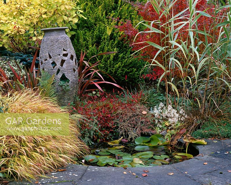 Granite urn resting in autumnal border beside small pond, Designer - Brian Cross at Lakemount, Ireland