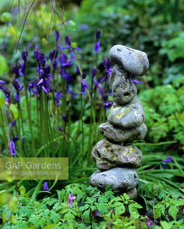 Sculpture made from a pile of stones with Hyacinthoides non-scripta - bluebells in background 