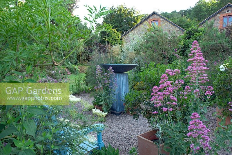 Seating area with contemporary water feature within borders. Selfseeded valerian in gravel