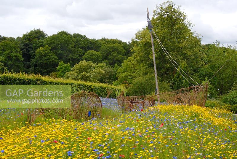 A meadow of flowering annuals with a pirate ship and a whale created from woven willow in the Pirates and Mermaids Garden at The RHS Gardens Harlow Carr