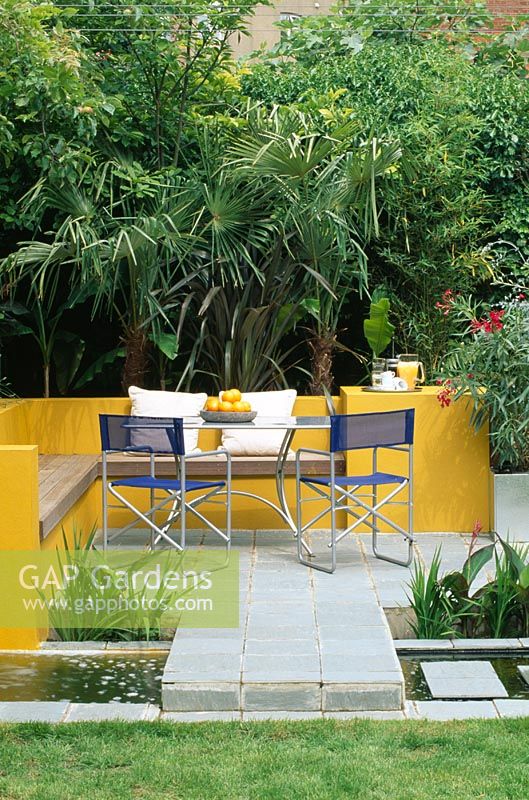 Aluminium table and chairs on patio surrounded by yellow rendered walls and rill with Oleander, Trachycarpus