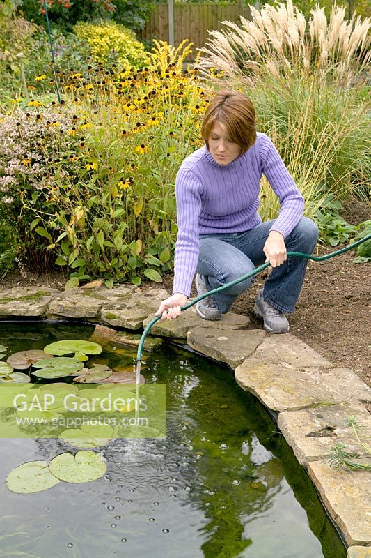 Woman spraying water from hosepipe onto surface of pond water, to top up pond and increase oxygen in water through bubbling