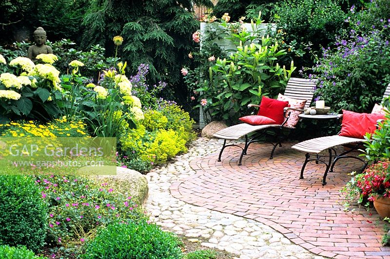 Two reclining chairs with view of a mixed border including Alchemilla mollis, Hydrangrea and a Buddah statue