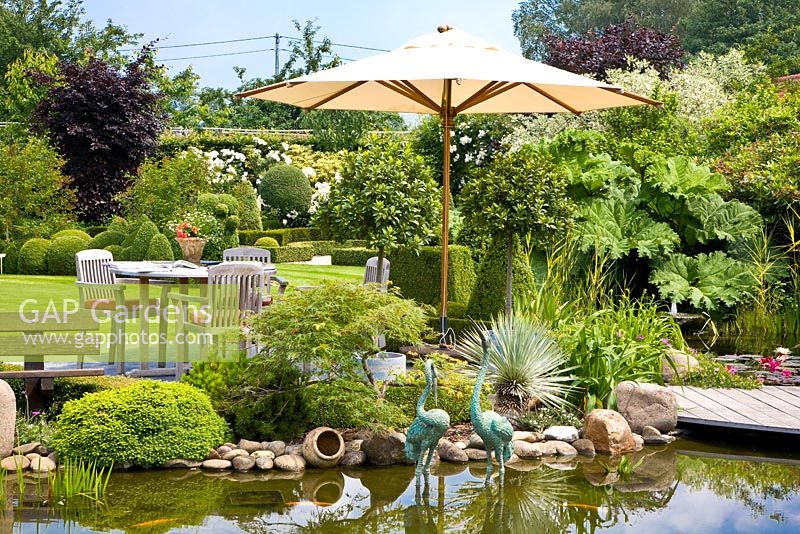 Sitting area with umbrella beside pond with heron statues