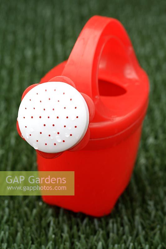 Child's plastic watering can on astroturf lawn