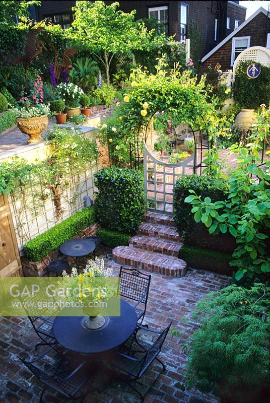 Overview of urban courtyard garden with brick paved terrace with table and chairs.  
Steps and arched gateway to raised patios - San Francisco, California, USA    

