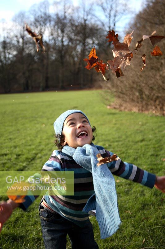 Laughing boy throwing Autumn leaves up in the air 