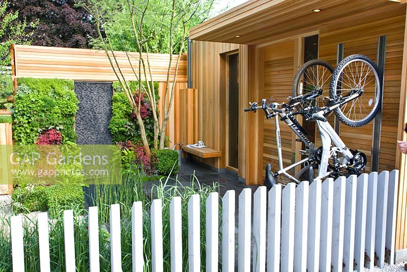 Bikes in bike rack in modern garden with living green wall with planting including ferns and Heuchera beside a vertical basalt water wall and plunge pool in The Children's Society Garden, Designed by Mark Gregory, Sponsor - The Co-operative, Chelsea Flower Show 2008
