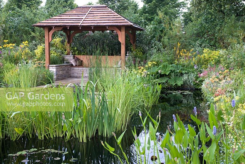 Wooden pavilion overlooking pond with marginal and moisture-loving plants - The World of Water Garden, RHS Hampton Court Flower Show 2008