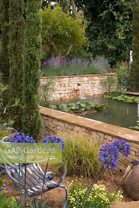Seating area overlooking raised pond with water feature and Agapanthus africanus in foreground - The Dorset Water Lily Garden, RHS Hampton Court Flower Show 2008
