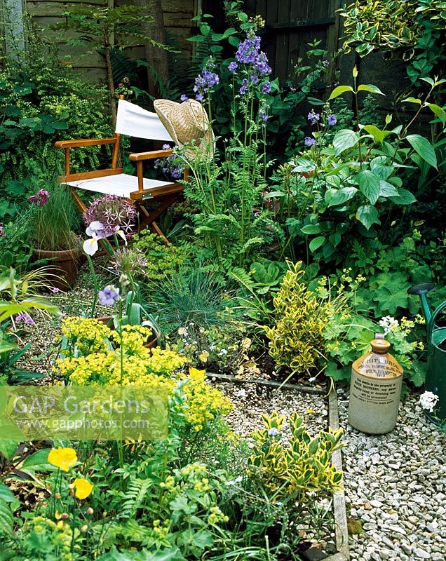 Mixed herbaceous beds with gravel pathway leading to director's chair in quiet corner of the garden