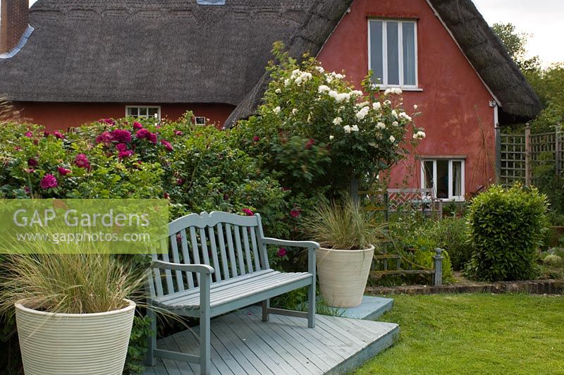 Simple wooden bench on raised decking, flanked by two large containers of ornamental grasses - Smallwood Farmhouse, Suffolk