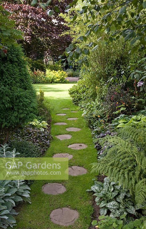 Long grass path with wooden stepping stones between borders of mature trees, shrubs and summer flowering perennials at Lilac Cottage, Staffordshire NGS