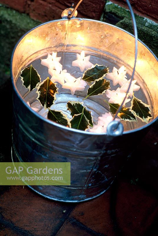 Metal bucket filled with water, lit floating star shaped candles and holly leaves