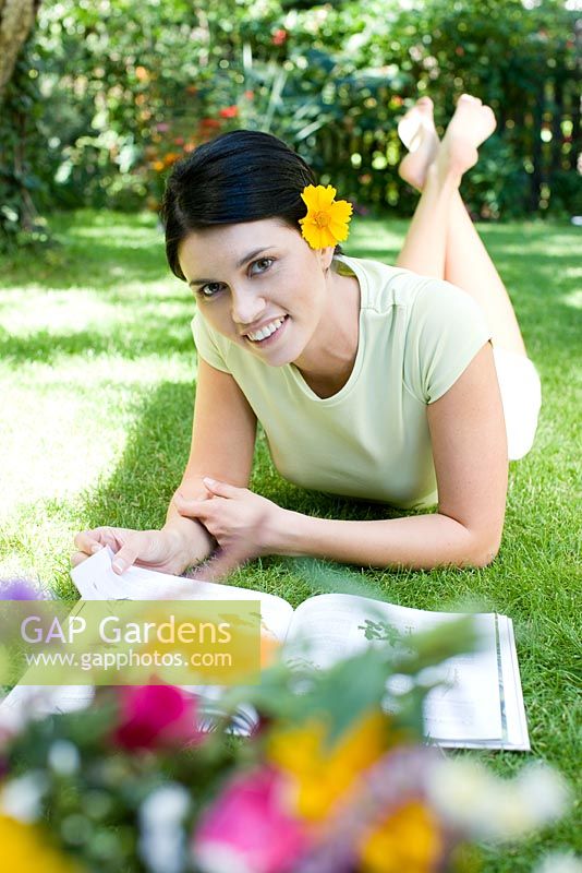 Woman lying on lawn looking at magazine with yellow flower behind her ear