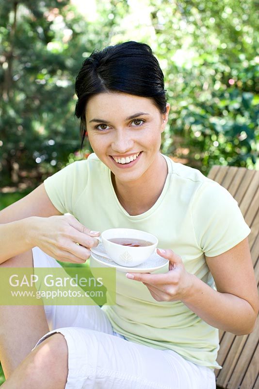 Woman sitting drinking cup of tea on sunlounger in garden