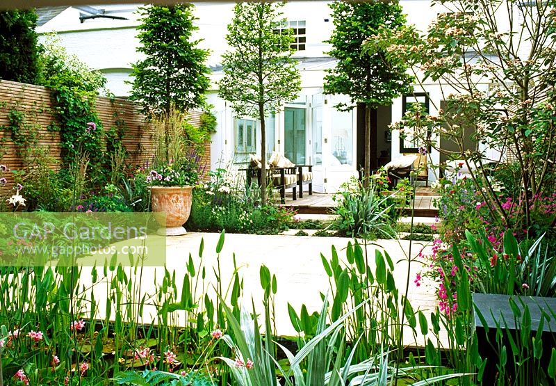 From this pale green, furnished garden apartment, sliding doors open onto an interior courtyard. The space is divided by pleached hornbeams and boarders of delicate perennials and including a stip shaped pond.