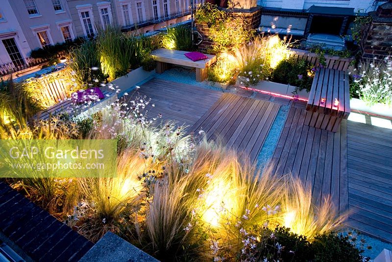 Decked terrace at night with pink and white led lighting and blue glass gravel - Roof garden, Holland Park, London