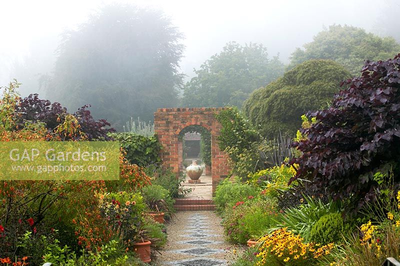Hot Borders. Misty summer morning at Cloudehill gardens, Olinda, Victoria, Australia. Perennial borders, with Eucalyptus trees as backdrop. Arts and crafts style garden, owned and created by Jeremy Francis.