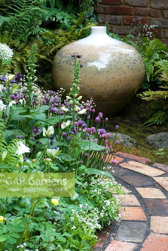 Glazed pot by John Stroomer surrounded by Aquilegia vulgaris 'Nivea', Allium 'Mont Blanc', Digitalis, Chives and Dicentra, next to a curved brick path. Pottering in North Cumbria, sponsored by University of Cumbria, Cumbrian Homes Ltd, Copeland Borough Council - Silver Flora medal winner for Courtyard Garden at RHS Chelsea Flower Show 2009