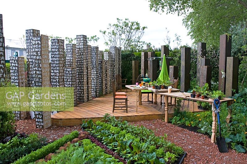 Outdoor dining area with decking, raised vegetable beds and tables and chairs made from recycling materials. The Key Garden, sponsored by Eden Project in partnership with The Homes and Communities Agency, Communities and Local Government, London Employer Accord - Silver medal winner at RHS Chelsea Flower Show 2009