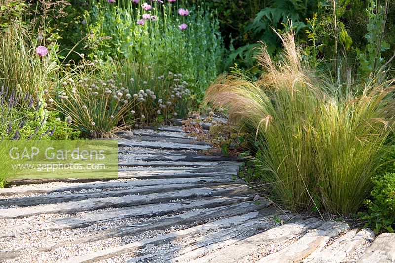 Old wooden boards used to create sweeping path in coastal-look garden with gravel in between