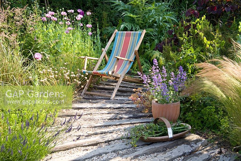 Deck chair in coastal-look garden, with trug and container with Nepeta