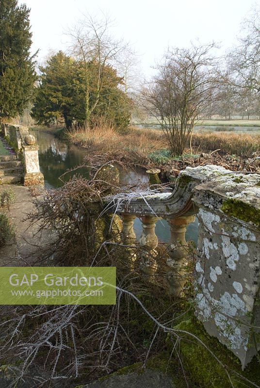 Stone steps and balustrades with Cotoneaster, leading down to river, Heale House Gardens, Wiltshire in frost