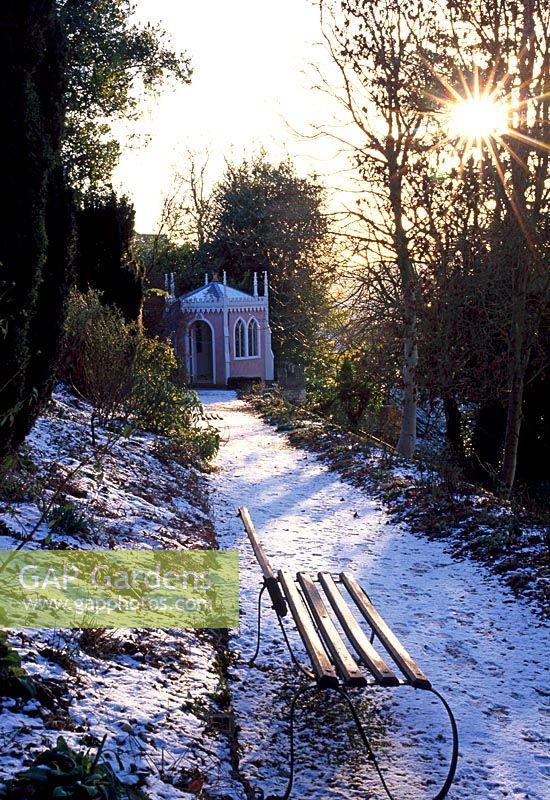 Bench and snow covered path leading to The Eagle House with sunburst - Painswick Rococo Garden, Painswick, Gloucestershire in February