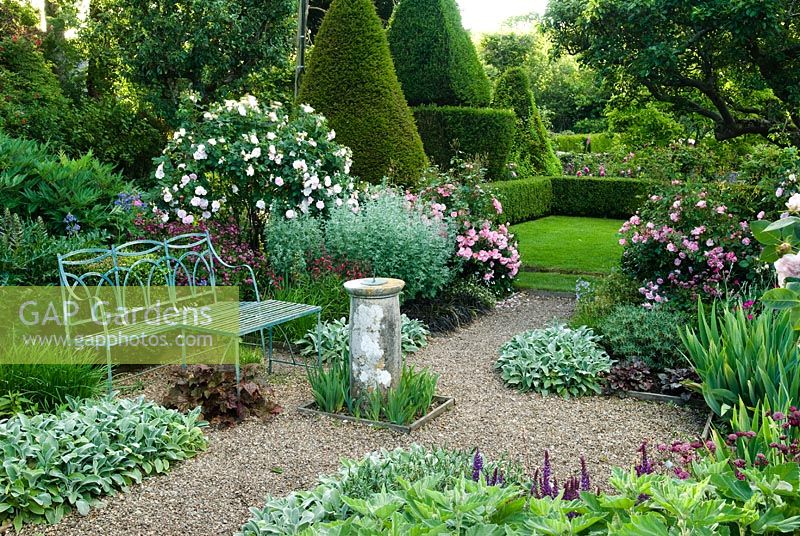 Formal garden with blue painted wrought iron bench, old sundial, gravel paths, roses, herbaceous perennials and view to lawns with box hedging and Yew topiary - Cerne Abbas, Dorset