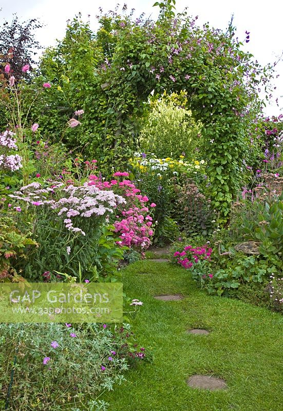 Lawn with stepping stone borders of herbaceous perennials with flowers in profusion, packed into an idyllic English cottage garden, in summer at Grafton Cottage (NGS) Barton-under-Needwood Staffordshire