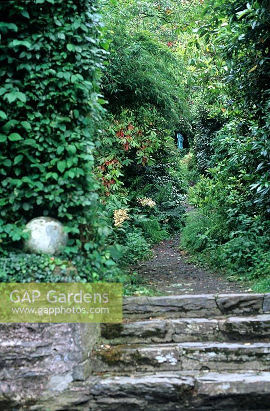 Stone steps leading to pathway through shrubs to a tromp l'oeil at Portmeirion, Wales