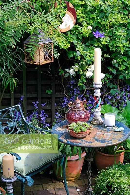 Romantic and atmospheric scented seating area backed by honeysuckle, roses and clematis with suspended lantern and mobiles and surrounded by plants in pots