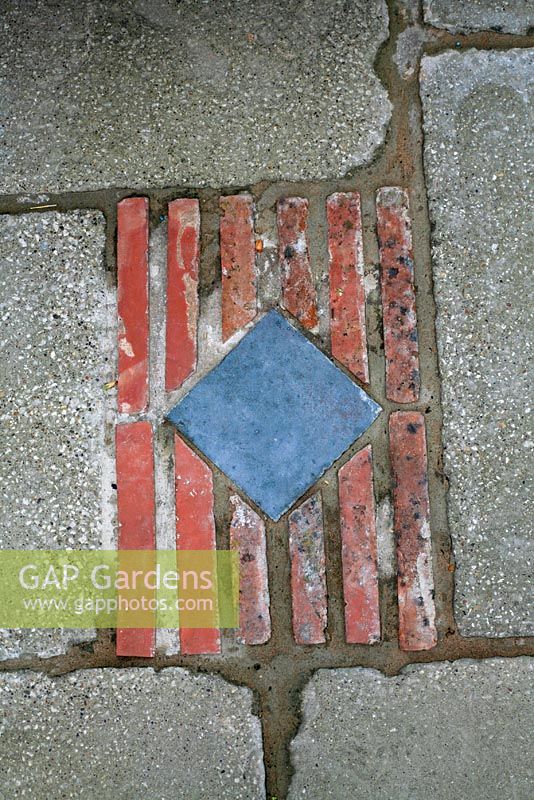 Marijke's garden. Decorative insert of a blue tile and red tiles on edge in a slabbed patio