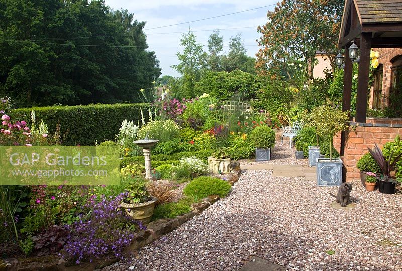 A plant lovers cottage garden with herbaceous perennials, metal containers with shaped box and hedging, a sun-dial with gravel path at Coley Cottage, NGS, Little Haywood, Staffordshire 
