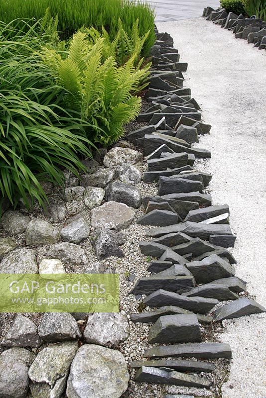Suburban family garden for restored Art Deco house. Paths made with white sand and cement. Close up of jagged slate pieces imitating the shoreline.