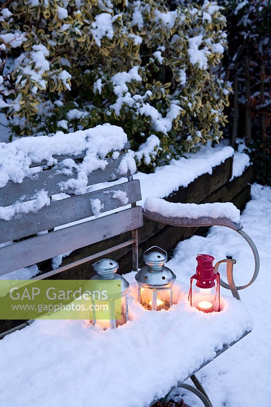 Three tea light candle lanterns set in snow on garden bench