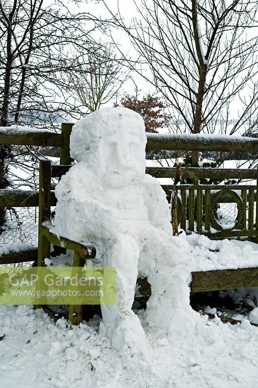Snowman made by children, sitting on garden bench
