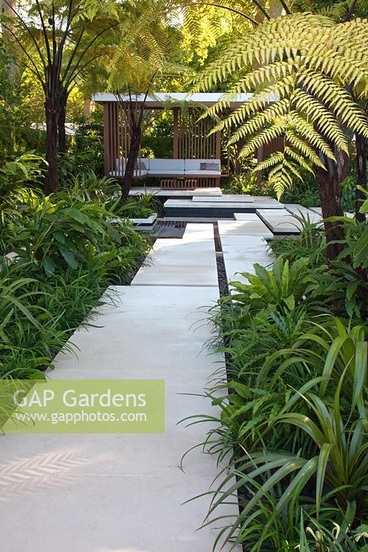 Large paved stepping stones cross water towards a pavilion bordered by tropical planting and tree ferns Cyathea latebrosa. The Tourism Malaysia Garden, Gold medal winner, RHS Chelsea Flower Show 2010 
 