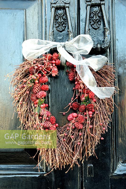 Autumn wreath of pine cones and berries, tied with a white ribbon, hanging from a cast iron door knocker 